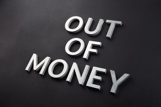 the words out of money laid with white brushed metal letters on flat matte black surface in diagonal perspective with selective focus