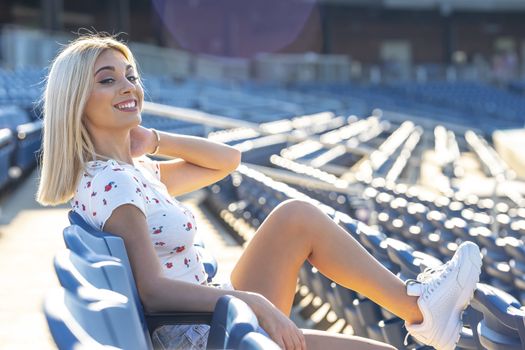A gorgeous young blonde model poses outdoors while enjoying a summers day at a stadium before a game