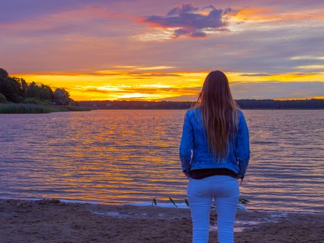 Portrait of young beautiful girl Watching sunset on the beach. Backview. Copy space. Image for wallpaper, background. Dramatic sky