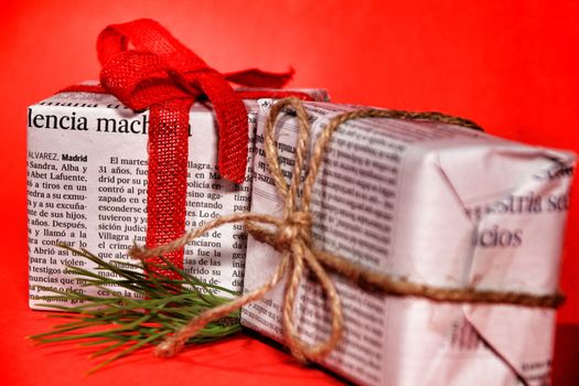 Gifts wrapped in old newspaper with red bow and rope on red background