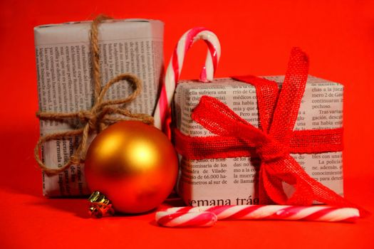 Gifts wrapped in old newspaper with red bow and rope on red background