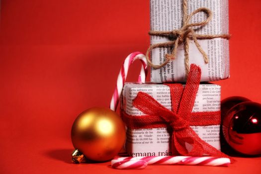 Gifts wrapped in old newspaper with red bow and rope on red background