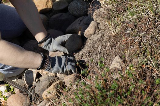 In protective gloves, a young teenager cleans weeds from places where ornamental plants and shrubs grow.
