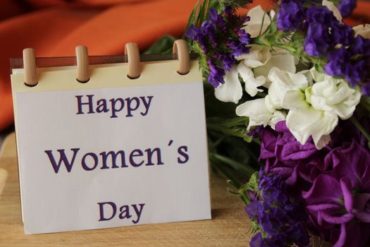 Purple and white liliums and helichrysum flowers sent on Womens Day. Open notebook with Happy Womens Day message