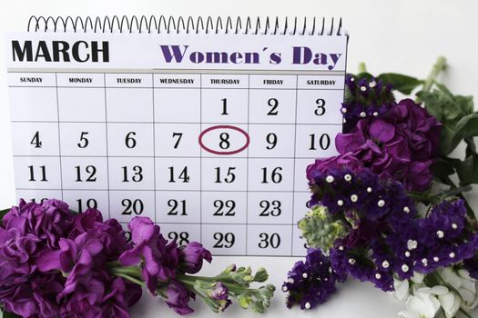 Purple and white liliums and helichrysum flowers and calendar with marked Womens Day on white background.