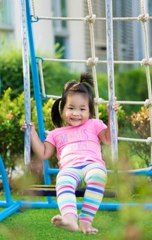 Little girl in pink dress sitting on a swing in the playground
