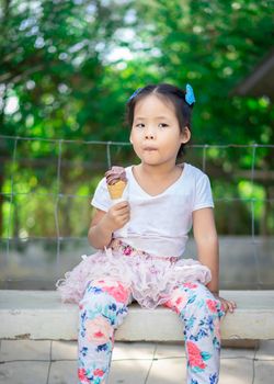 Asian little girl eating an ice cream outdoors with natural light blur background