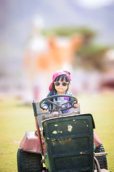 Cute asian little girl wear sunglasses playing by driving a old tractor in farm
