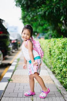 Portrait of happy little girl with backpack standing on footpath in the park