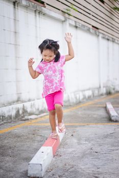Little asian girl walking on the curb and trying to keep her balance