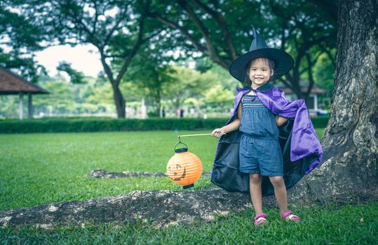 Little girl in a witch costume holding a lamp in halloween