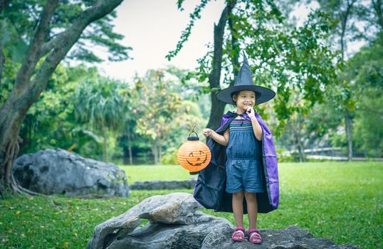 Little girl in a witch costume holding a lamp in halloween