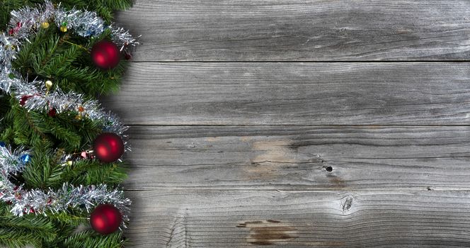 Merry Christmas and Happy New Year holiday concept with silver tinsel and red ball ornaments on rustic wood 