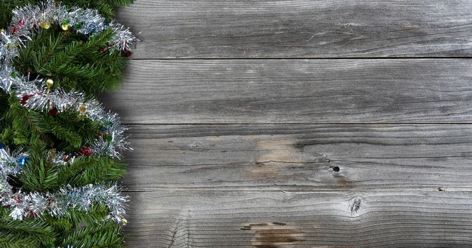 Merry Christmas and Happy New Year holiday concept with silver tinsel on top of fir branches on left side of rustic wood