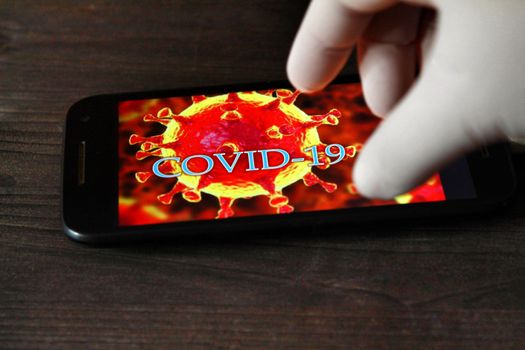 Madrid, Spain- April 23, 2020: Hand in surgical glove pointing at a mobile phone with picture of covid-19 word written on it