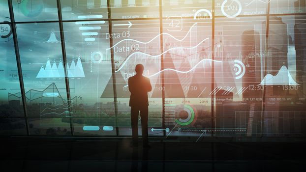 Businessman silhouette in a dark office in front of a large array of infographics.