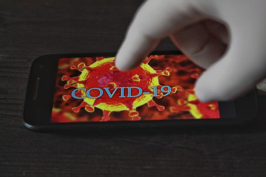 Madrid, Spain- April 23, 2020: Hand in surgical glove pointing at a mobile phone with picture of covid-19 word written on it