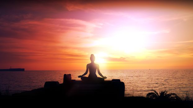 Silhouette of a woman meditating against a sunset in the ocean.