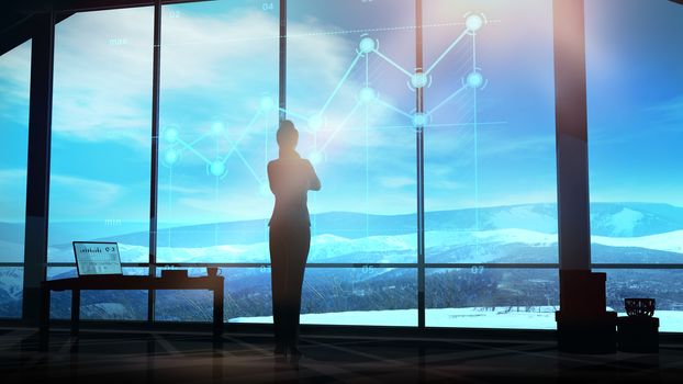 Silhouette of a businesswoman stands in front of a panoramic office window overlooking a winter mountain landscape and looks at holographic infographics.