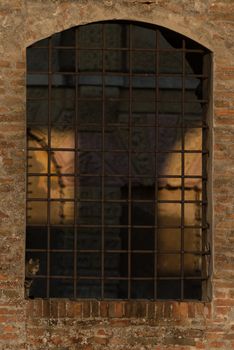 A kitten looks out from the grate of a window of an ancient building illuminated by the warm morning lights