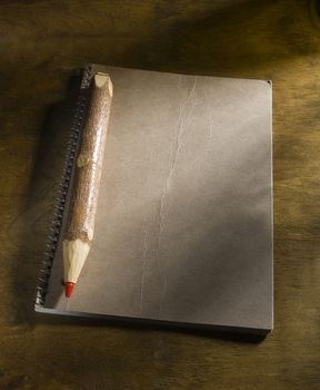 Large wooden pencil with red lead and notepad on the table