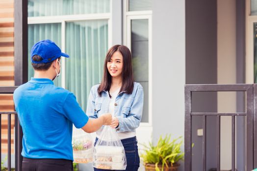 Asian young delivery man wear face mask he making grocery service giving rice food boxes plastic bags to woman customer receiving door at house after pandemic coronavirus, Back to new normal concept