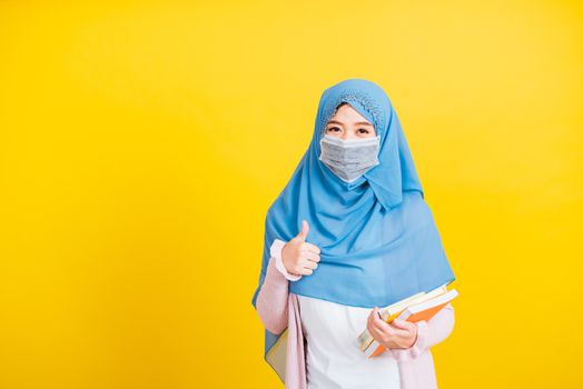 Asian Muslim Arab, Portrait of beautiful young woman religious wear veil hijab and face mask protective to prevent coronavirus hold books on hand and show finger thumb up for good sign Back to college