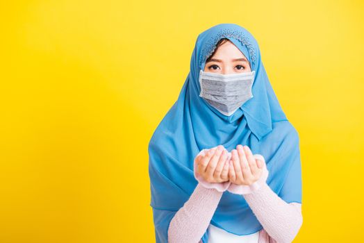 Asian Muslim Arab, Portrait beautiful young woman religious wear veil hijab and face mask protect to prevent coronavirus she henna decorated hands praying to Allah God, isolated on yellow background