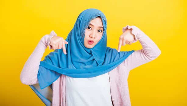 Asian Muslim Arab, Portrait of happy beautiful young woman Islam religious wear veil hijab funny smile she positive expression points finger down with hands, studio shot isolated yellow background