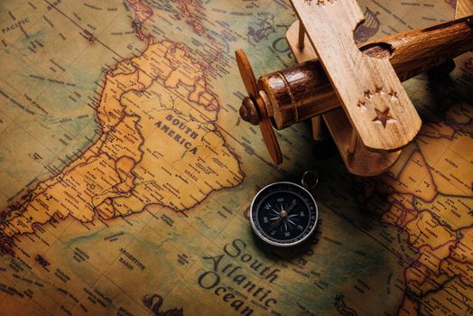 Old compass discovery and wooden plane on vintage paper antique world map background, Retro style cartography travel geography navigation, Columbus Day concept