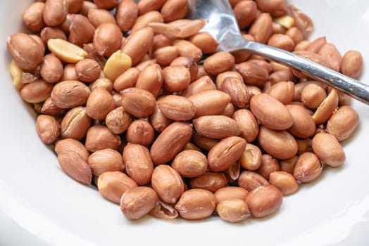 The close up of brown roasted peanuts snack food on small white bowl.