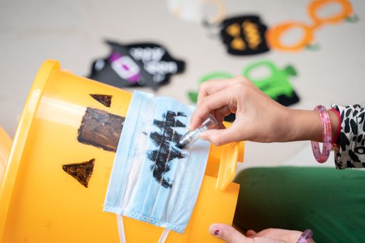 Close up hands, Kid preparing Treak or treat DIY box by drawing on medical face mask for Halloween - concept of halloween preparation and decoration at home