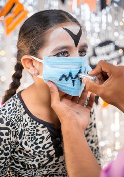 kid getting ready or preparing for Halloween by painting on medical face mask - concept of holiday, halloween, and childhood festival celebration and preparation