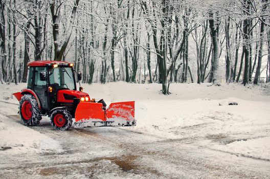 Excavator cleans the streets of large amounts of snow in city. Tractor with snowplow removing snow during heavy snowfall. Winter time street maintenance in hard weather conditions