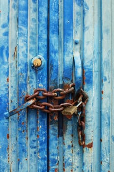 Old and colorful metallic door and closed with rusty chain and padlock