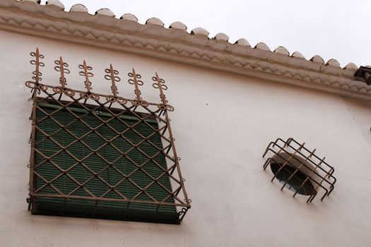 Window with wrought iron details and green blind on white stone facade in Villanueva de los Infantes, Castile-la Mancha, Spain