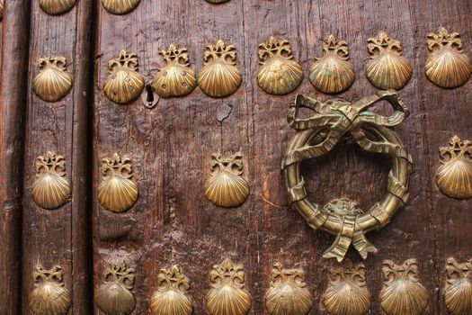 Old door with golden wrought iron details with figures of shells. Rusty and antique lock in the corner.