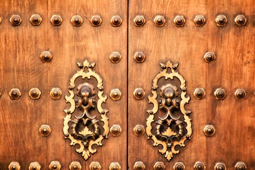 Forged metal vintage golden door knocker on brown wooden door in Cordoba, Spain