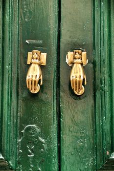 Door knockers with hand shape on green wooden door