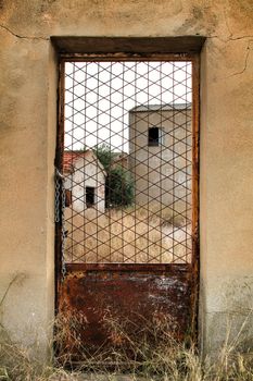 Old abandoned factory seen through rusty metal door in Spain