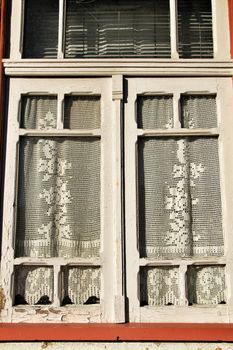 Old wooden window painted in white with crochet curtain in Porto, Portugal.
