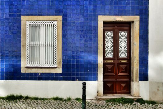 Old and colorful wooden door with iron details and blue tiled facade in Lisbon, Portugal