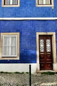 Old and colorful wooden door with iron details and blue tiled facade in Lisbon, Portugal