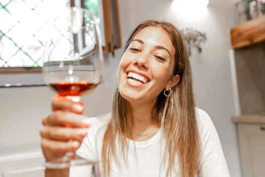 Cute young caucasian blonde woman toasting with red wine glass looking at the camera at home - New normal remote conference communication by online technology for the Coronavirus pandemic