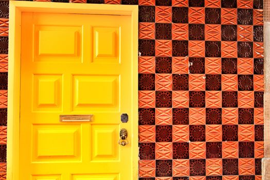 Yellow door with door knocker lion shaped and brown tiled wall in Lisbon