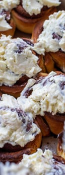 Delicious round rolls of dough with cinnamon on top smeared with sweet cream on a baking sheet after the oven. I cook buns at home in the oven.