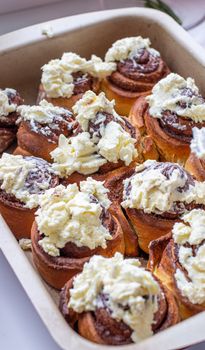 Delicious round rolls of dough with cinnamon on top smeared with sweet cream on a baking sheet after the oven. I cook buns at home in the oven.