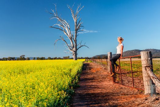 Country woman basking in the spring sunshine looking out over the fields of canola flowering bright yellow