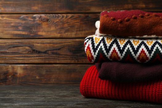 Pile of sweaters on wooden background, space for text