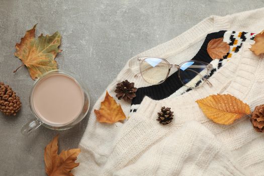 Concept of autumn wear with sweaters and coffee on gray background